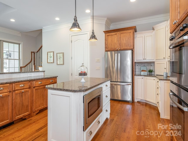 kitchen with hanging light fixtures, ornamental molding, stainless steel appliances, light hardwood / wood-style floors, and a center island