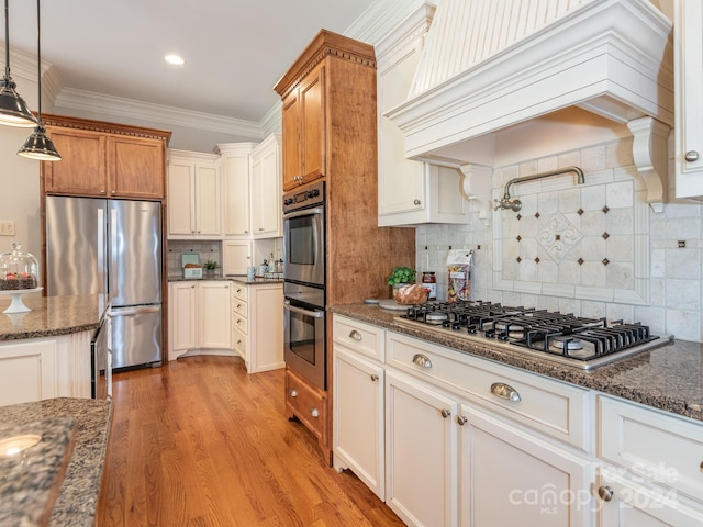 kitchen with hanging light fixtures, backsplash, appliances with stainless steel finishes, premium range hood, and light hardwood / wood-style floors