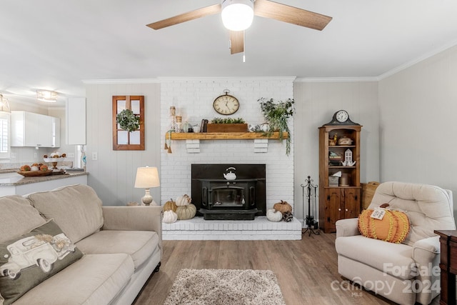 living room featuring light hardwood / wood-style floors, a wood stove, ceiling fan, and crown molding