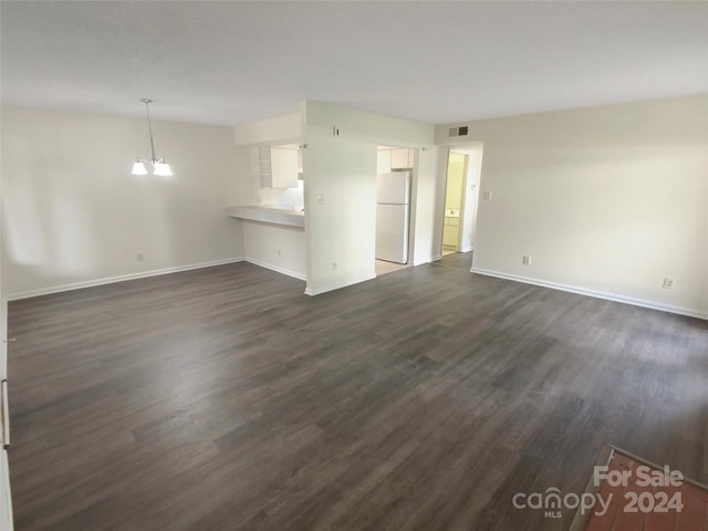 unfurnished living room featuring a notable chandelier and dark hardwood / wood-style floors