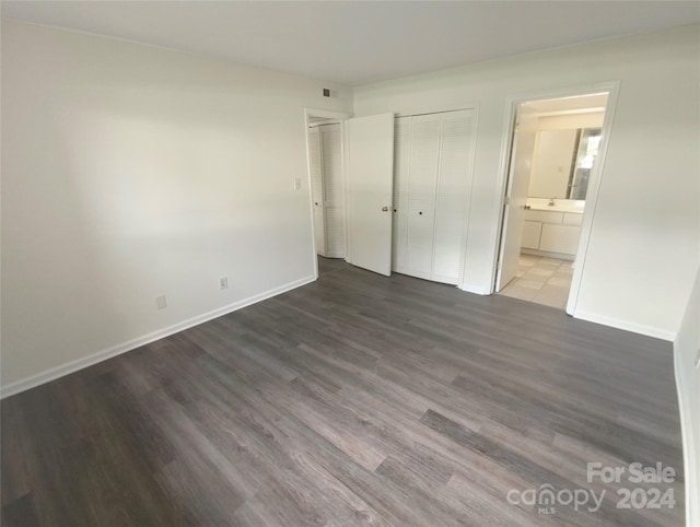 unfurnished bedroom with a closet, ensuite bathroom, and dark hardwood / wood-style floors