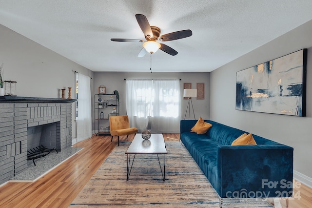 living room with ceiling fan, a textured ceiling, a fireplace, and hardwood / wood-style floors