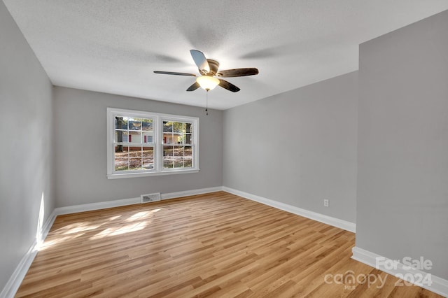 unfurnished room with a textured ceiling, light wood-type flooring, and ceiling fan