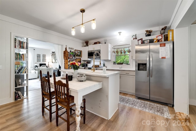 kitchen featuring appliances with stainless steel finishes, white cabinets, light wood-type flooring, and pendant lighting