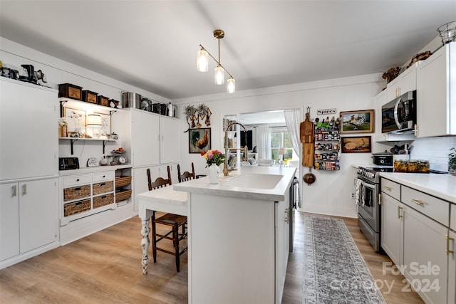 kitchen with white cabinets, hanging light fixtures, an island with sink, appliances with stainless steel finishes, and sink