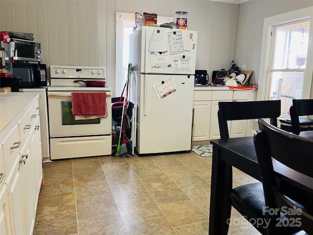 kitchen featuring white appliances, white cabinets, and wood walls