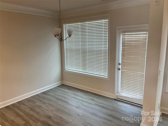 unfurnished dining area with ornamental molding, a notable chandelier, and wood-type flooring