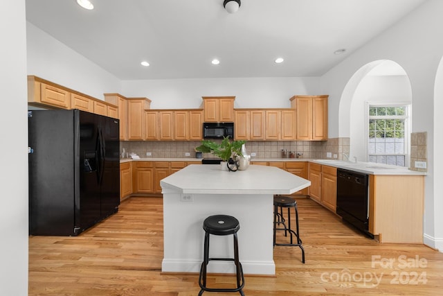 kitchen with light hardwood / wood-style flooring, a center island, black appliances, and a breakfast bar