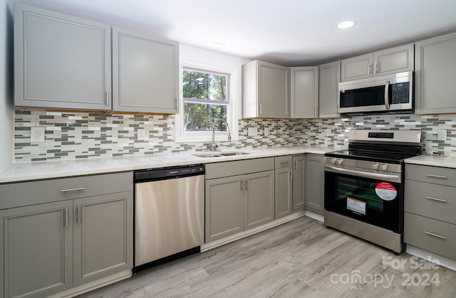 kitchen featuring stainless steel appliances, sink, light wood-type flooring, gray cabinets, and tasteful backsplash