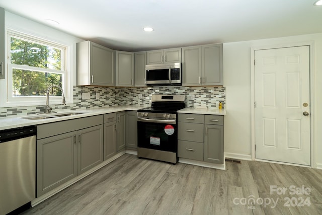 kitchen featuring decorative backsplash, light hardwood / wood-style flooring, sink, gray cabinetry, and stainless steel appliances