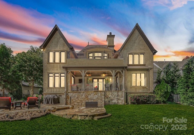 back house at dusk featuring a patio area, a balcony, and a yard