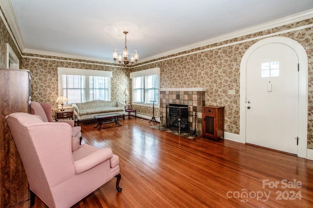 living room with a tiled fireplace, hardwood / wood-style flooring, a baseboard heating unit, crown molding, and a notable chandelier