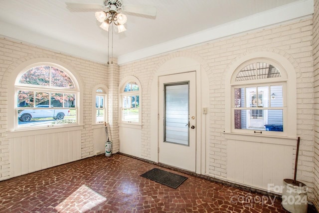 foyer entrance with brick wall, crown molding, and ceiling fan