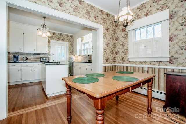 dining area featuring sink, a baseboard radiator, a notable chandelier, ornamental molding, and light hardwood / wood-style flooring