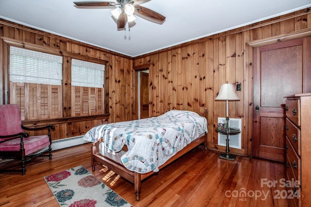 bedroom featuring wooden walls, a baseboard heating unit, ornamental molding, hardwood / wood-style floors, and ceiling fan