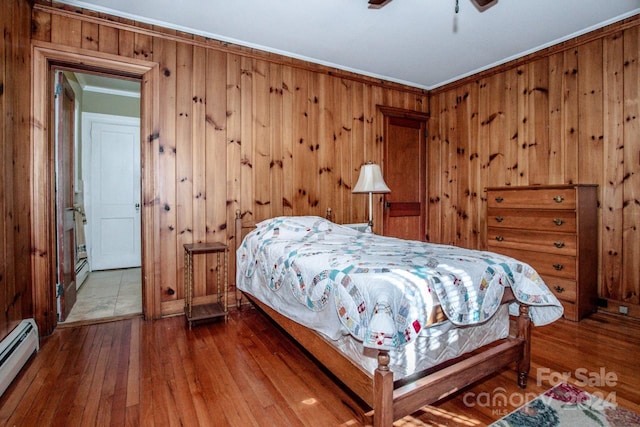 bedroom with hardwood / wood-style floors, a baseboard heating unit, ceiling fan, wood walls, and crown molding