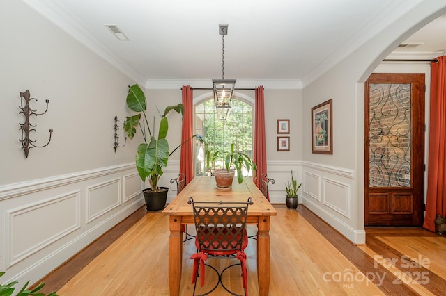 dining space with ornamental molding, arched walkways, and light wood finished floors