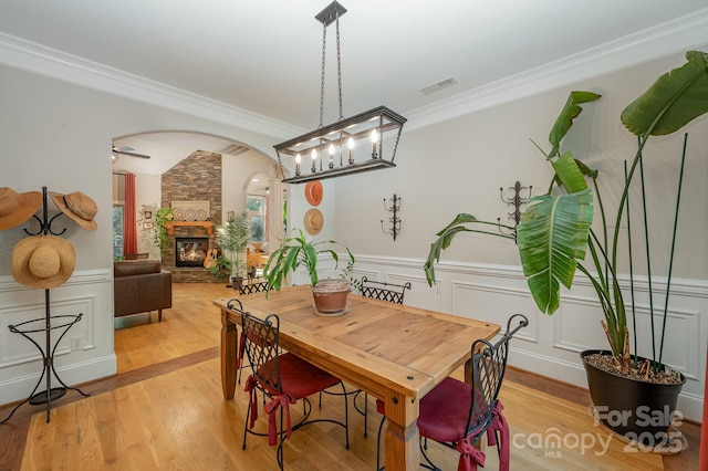 dining room with visible vents, arched walkways, ornamental molding, a stone fireplace, and light wood-type flooring