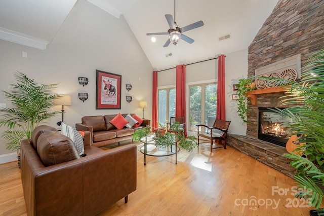 living room featuring light wood-type flooring, high vaulted ceiling, visible vents, and a stone fireplace