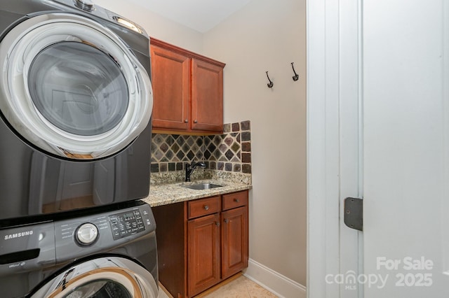 clothes washing area with cabinet space, stacked washer / dryer, light tile patterned flooring, a sink, and baseboards