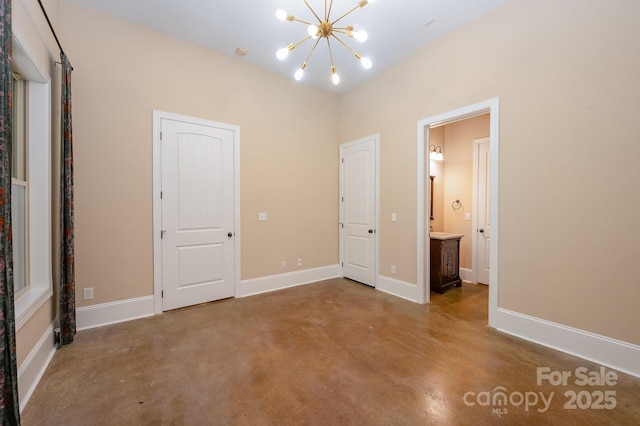 unfurnished bedroom with finished concrete floors, a notable chandelier, ensuite bath, and baseboards