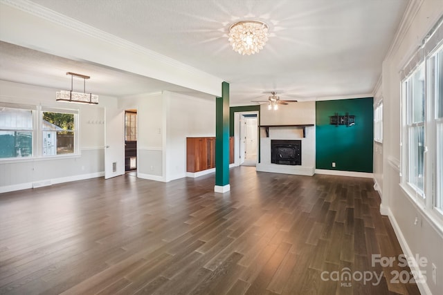 unfurnished living room featuring ceiling fan with notable chandelier, crown molding, and dark wood-type flooring