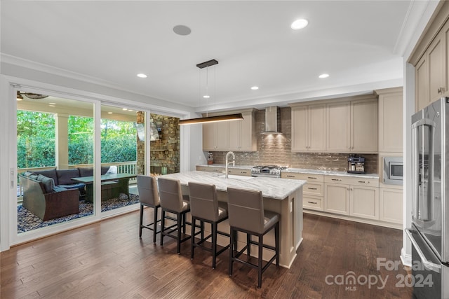 kitchen with dark hardwood / wood-style floors, wall chimney exhaust hood, an island with sink, decorative light fixtures, and appliances with stainless steel finishes