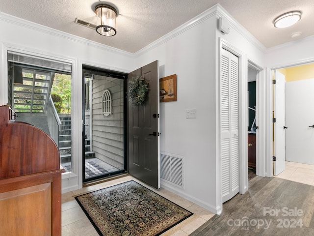 tiled entryway with ornamental molding and a textured ceiling