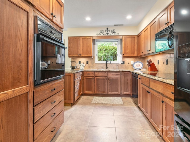 kitchen featuring black appliances, light stone countertops, sink, and tasteful backsplash