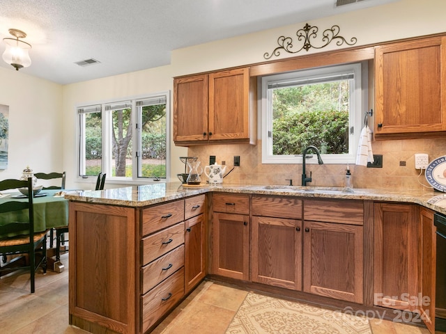 kitchen featuring sink, decorative backsplash, light stone countertops, a textured ceiling, and kitchen peninsula