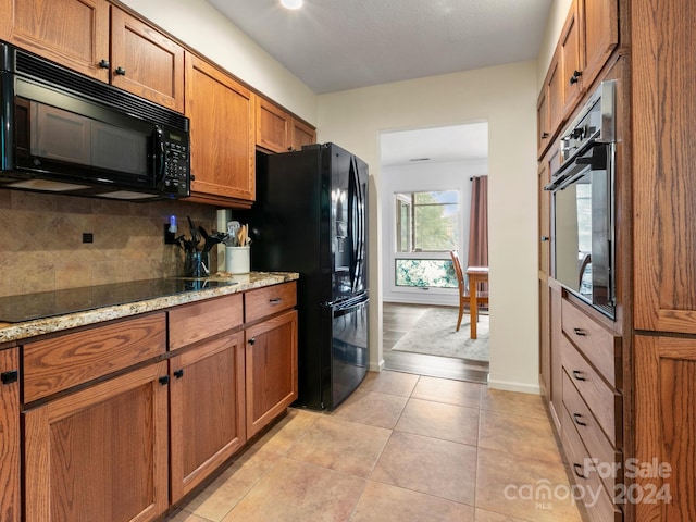 kitchen featuring black appliances, light stone countertops, backsplash, and light tile patterned floors