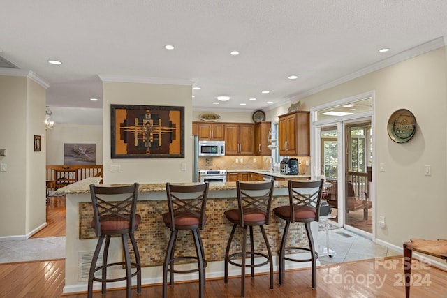 kitchen with light hardwood / wood-style floors, appliances with stainless steel finishes, a breakfast bar area, and light stone counters