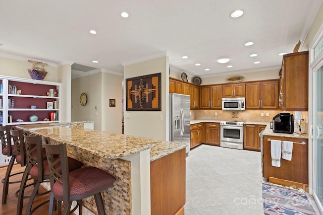 kitchen with crown molding, appliances with stainless steel finishes, tasteful backsplash, a kitchen breakfast bar, and light stone counters