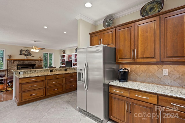 kitchen featuring a brick fireplace, stainless steel fridge, light stone counters, ornamental molding, and light tile patterned floors