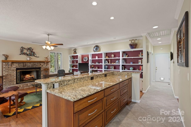 kitchen featuring a kitchen breakfast bar, crown molding, light tile patterned floors, light stone counters, and a fireplace