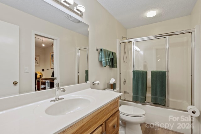 full bathroom featuring shower / bath combination with glass door, vanity, a textured ceiling, and toilet