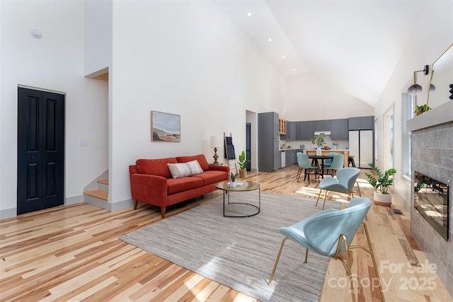 living room with a fireplace, high vaulted ceiling, and light hardwood / wood-style floors