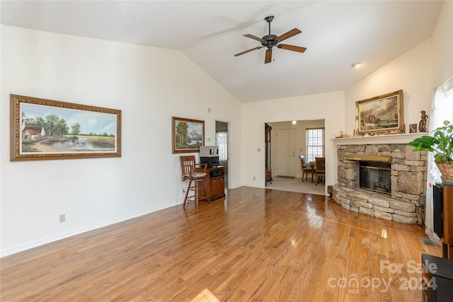 living room with a stone fireplace, high vaulted ceiling, light wood-type flooring, and ceiling fan