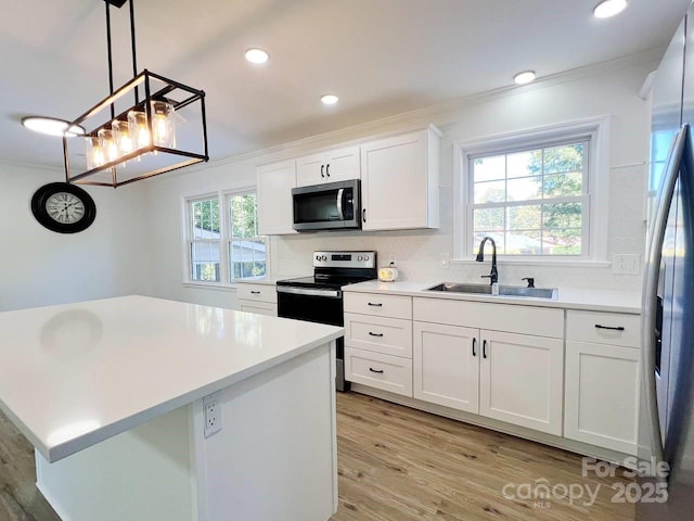 kitchen with stainless steel appliances, white cabinets, pendant lighting, ornamental molding, and sink