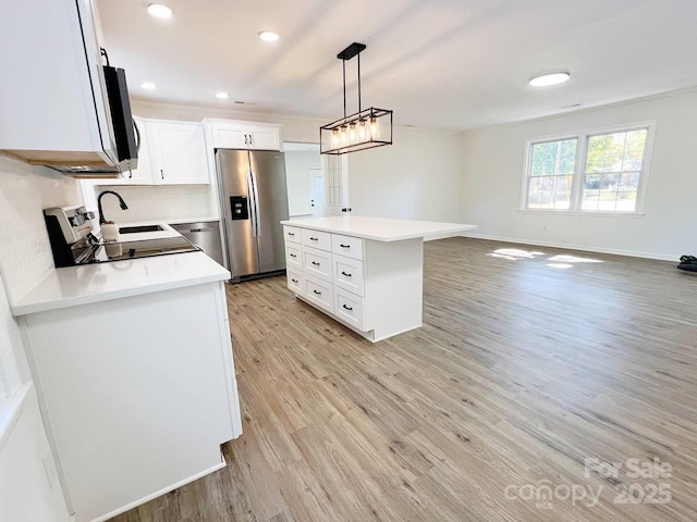 kitchen featuring appliances with stainless steel finishes, pendant lighting, a kitchen island, light wood-type flooring, and white cabinetry