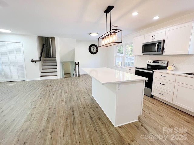 kitchen featuring appliances with stainless steel finishes, light hardwood / wood-style flooring, white cabinetry, pendant lighting, and a kitchen island