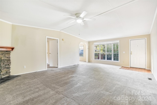 unfurnished living room with carpet, ceiling fan, vaulted ceiling, a stone fireplace, and crown molding