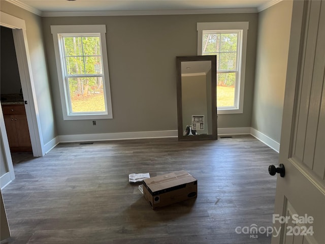 empty room with a healthy amount of sunlight, ornamental molding, and dark wood-type flooring