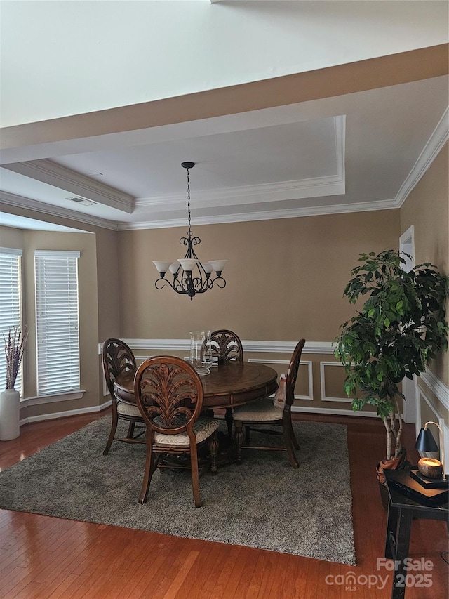 dining space with a notable chandelier, a tray ceiling, ornamental molding, and hardwood / wood-style floors