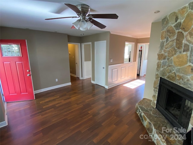 living room with crown molding, a stone fireplace, dark hardwood / wood-style flooring, and ceiling fan