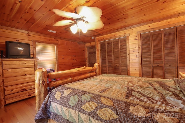 bedroom with wood ceiling, multiple closets, wooden walls, ceiling fan, and hardwood / wood-style floors