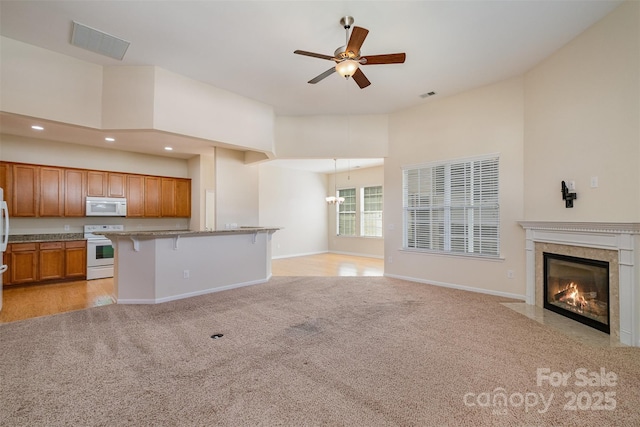 unfurnished living room with a high end fireplace, light colored carpet, ceiling fan, and a high ceiling