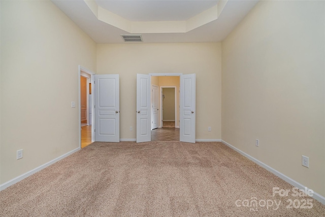 unfurnished bedroom featuring a tray ceiling, light carpet, and a high ceiling