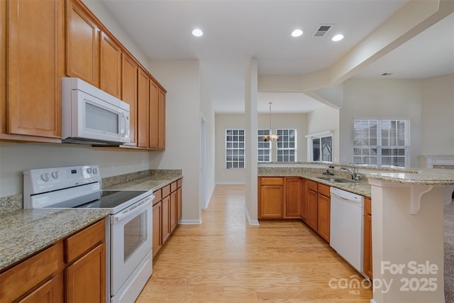 kitchen with a kitchen bar, sink, light wood-type flooring, white appliances, and light stone countertops