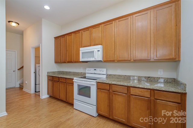 kitchen featuring white appliances, washer / dryer, light hardwood / wood-style floors, and light stone countertops